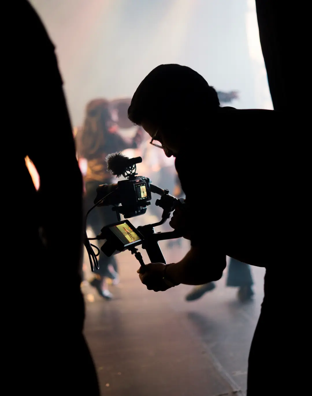 Cinegrafista em silhueta contra a fumaça do palco, com o monitor aceso